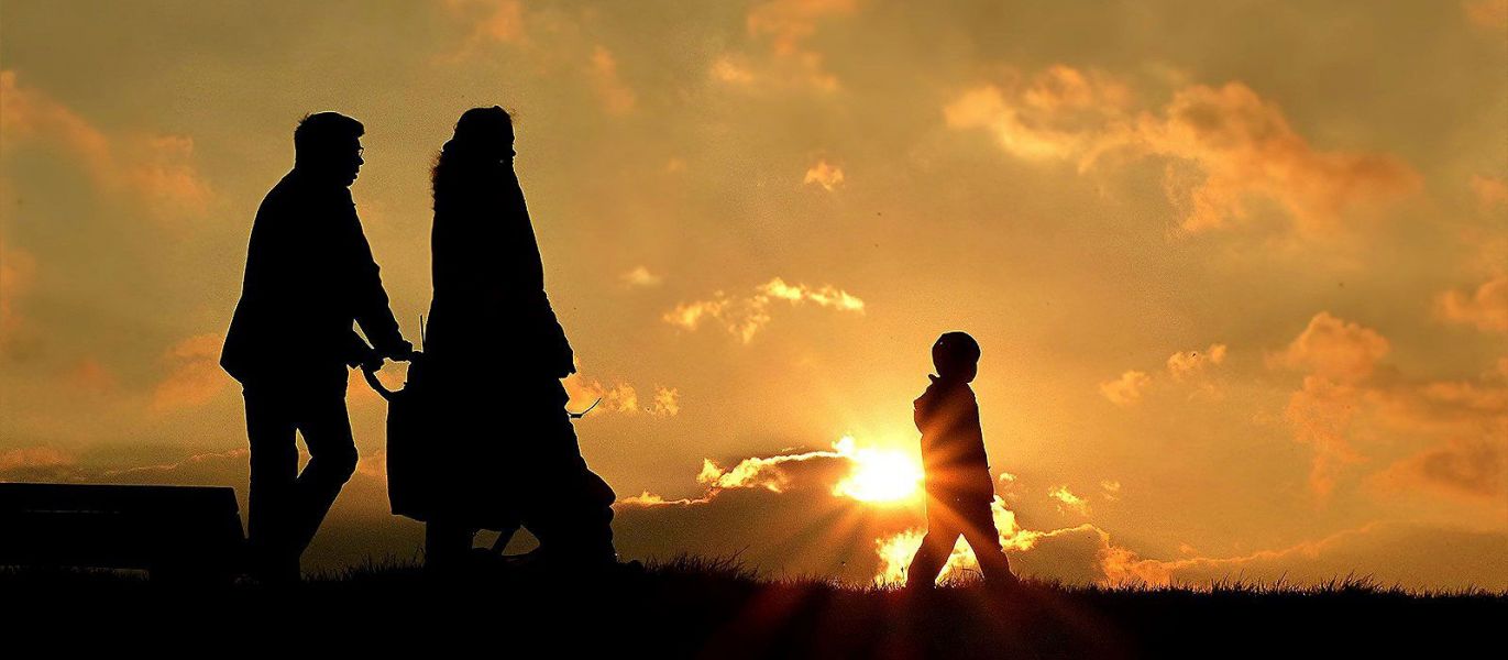 Eine Familie, bestehend aus Mutter, Vater und Kind, laufen bei Sonnenuntergang über eine Wiese